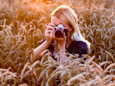 Abbildung Frau die mit Kamera in einem Feld sitzt und Fotos macht